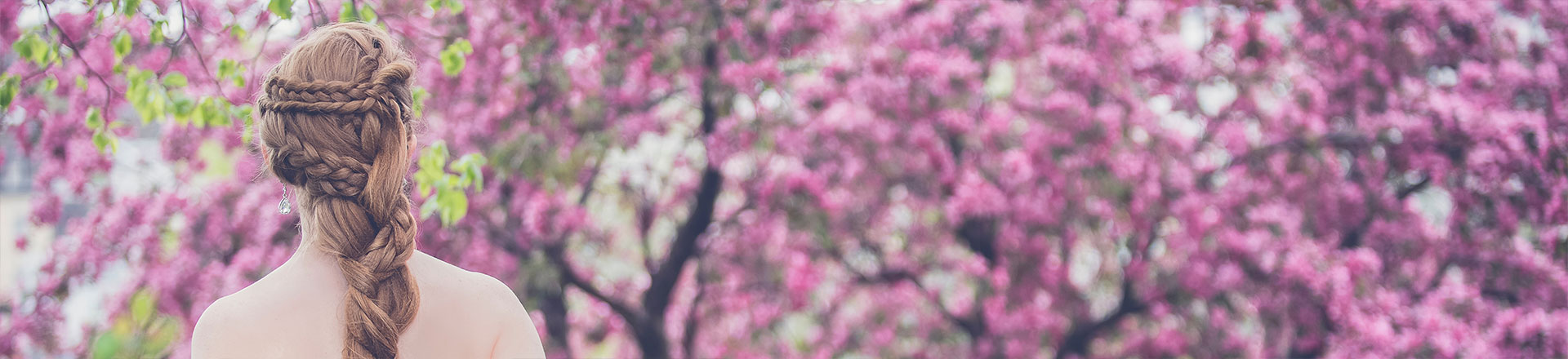 Braut mit langen braunen Haaren zum Zopf geflochten steht vor einer lila Blumenwiese